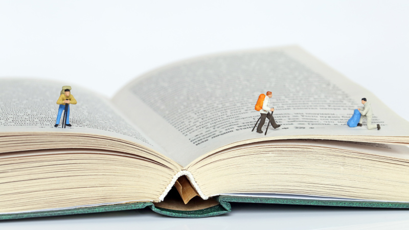 Kleine Plastik-Figuren wandern über ein aufgeschlagenes Buch